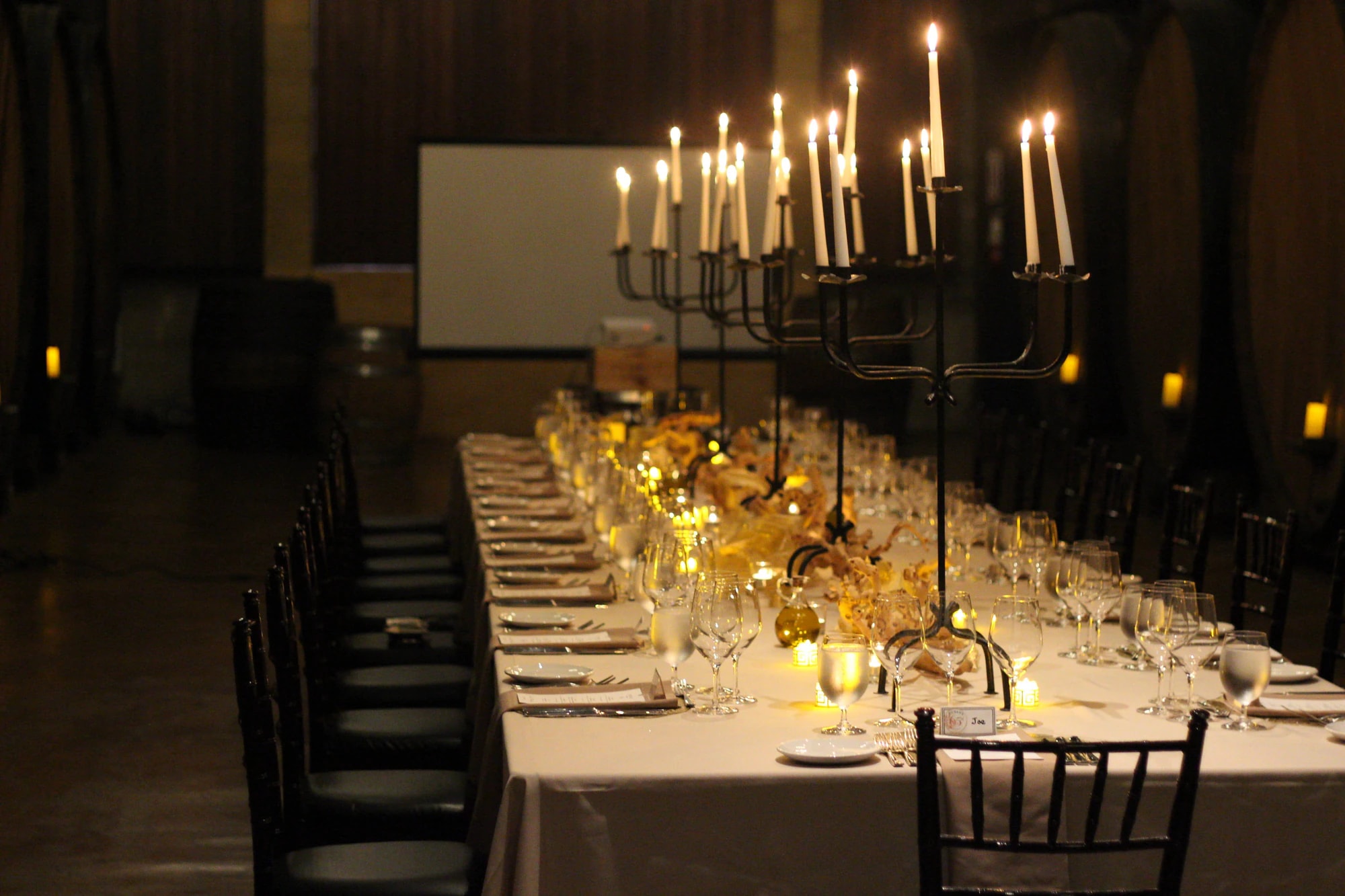 A long table set with candelabras in a barrel room, lit only by candlelight